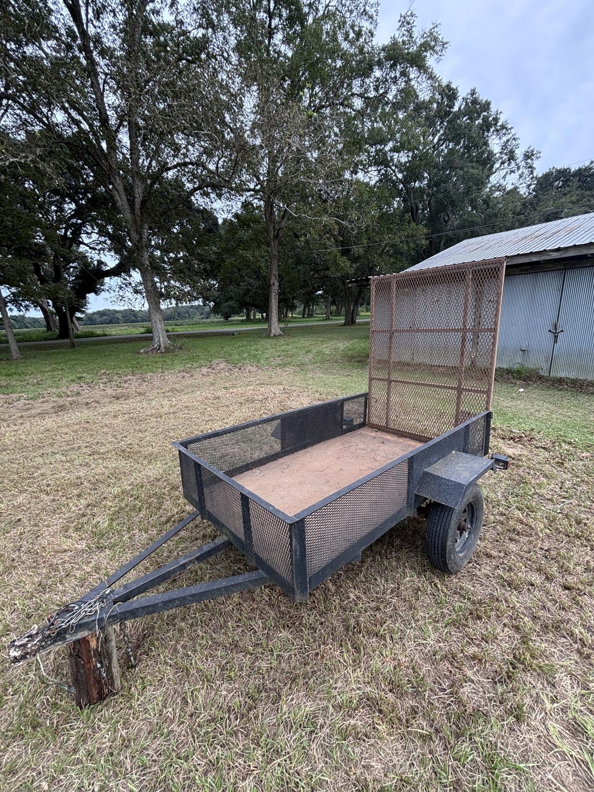 Three-quarter view of the 4 × 8 utility trailer with the ramp raised and trees behind