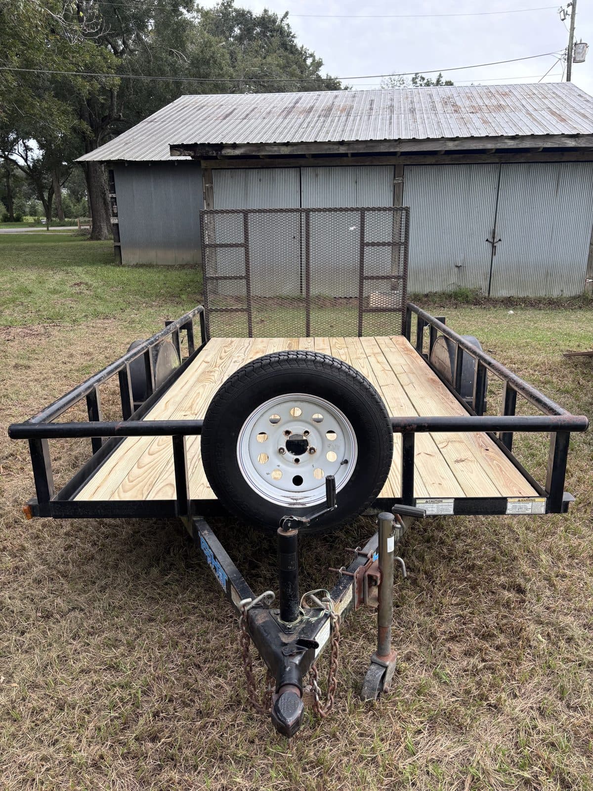 Front view of the 6 × 12 utility trailer down the tongue with a spare tire mounted, ramp gate raised, and new wood deck